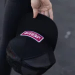 Hand holding the black Warrior Makers classic trucker hat with a pink JESUS patch, showing the mesh back panels