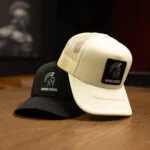 Cream and black Warrior Makers foam trucker hats stacked on a wood table, each with a Spartan helmet patch