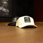 Cream Warrior Makers foam trucker hat with a Spartan helmet patch, shown on a wood table