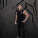 Man wearing a black Warrior Makers tank top and hat in front of a dark Spartan helmet backdrop