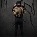 Woman with long blonde hair seen from behind wearing black Warrior Makers apparel and adjusting her hat in front of a dark Spartan helmet backdrop