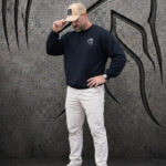 Man wearing an XXL Warrior Makers black crewneck sweatshirt and tan hat with khaki pants in front of a dark Spartan helmet backdrop