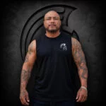 Man wearing an XL Warrior Makers black muscle tank cutoff with small chest logo in front of a dark Spartan helmet backdrop