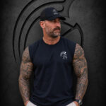 Man wearing an XXL Warrior Makers black muscle tank cutoff and black hat in front of a dark Spartan helmet backdrop