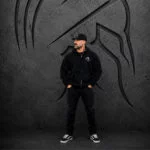 Man wearing an XXL Warrior Makers black zip-up hoodie, black pants and hat in front of a dark Spartan helmet backdrop
