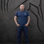 Man wearing an XL Warrior Makers navy blue t-shirt with small chest logo, standing in front of a dark Spartan helmet backdrop