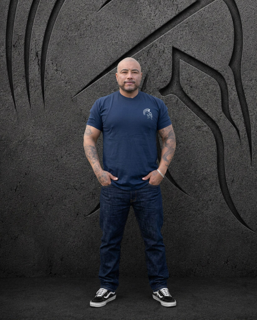 Man wearing an XL Warrior Makers navy blue t-shirt with small chest logo, standing in front of a dark Spartan helmet backdrop