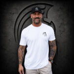 Man wearing an XXL Warrior Makers white t-shirt and black hat in front of a dark Spartan helmet backdrop