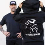 Man holding up the black Warrior Makers zip hoodie to show the Spartan helmet and WARRIOR MAKERS back print