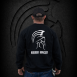 Back view of a man wearing a large Warrior Makers black crewneck sweatshirt with white Spartan helmet logo in front of a dark Spartan helmet backdrop