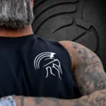 Close-up of the white Spartan helmet chest logo on a Warrior Makers men's black muscle tank worn by a tattooed man