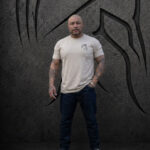 Man wearing an XL Warrior Makers tan t-shirt and jeans in front of a dark Spartan helmet backdrop